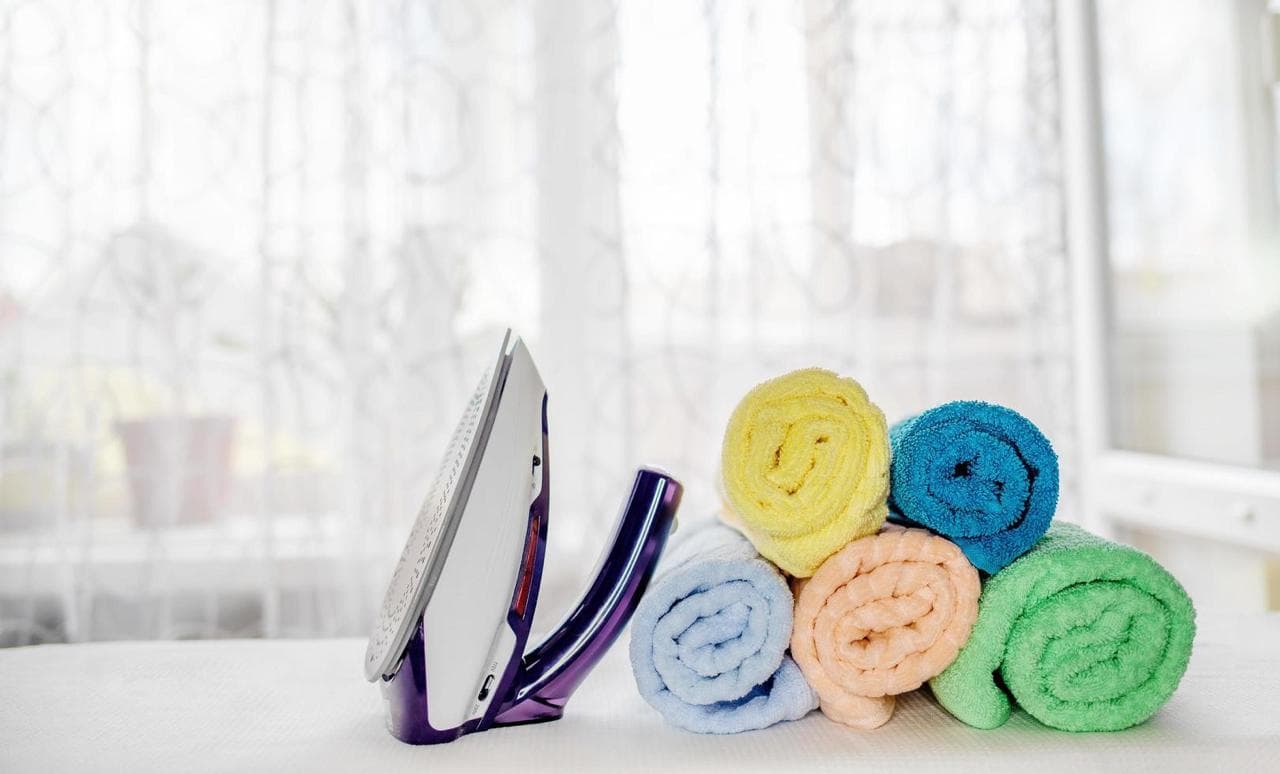 A professional carer smiling as she folds fresh laundry in a bright, clean home.
